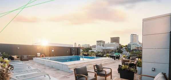 A rooftop pool area with a city skyline view, lounge chairs, and a small table.