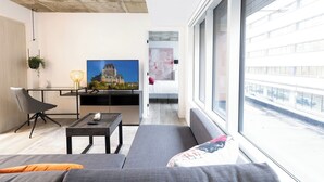 A modern living room with a flat-screen TV, a sofa, a coffee table, and a dining area with a table and chairs.