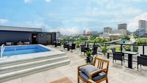 A rooftop pool area with a city view, outdoor seating, and a staircase leading to the pool.