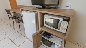 Eine kleine Küchenzeile mit Mikrowelle, Kühlschrank und einer Essecke mit einem Stuhl.