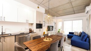 Une cuisine moderne avec des meubles blancs, une table à manger en bois et un canapé bleu dans l’espace salon.
