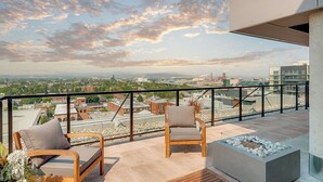Un balcon avec deux chaises en bois, un petit foyer et une vue sur la ville.