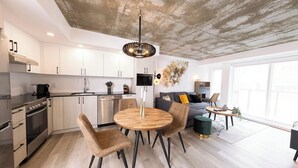 Una cocina moderna con armarios blancos, un comedor con una mesa redonda de madera y sillas, y una sala de estar con un sofá y una mesa de centro.