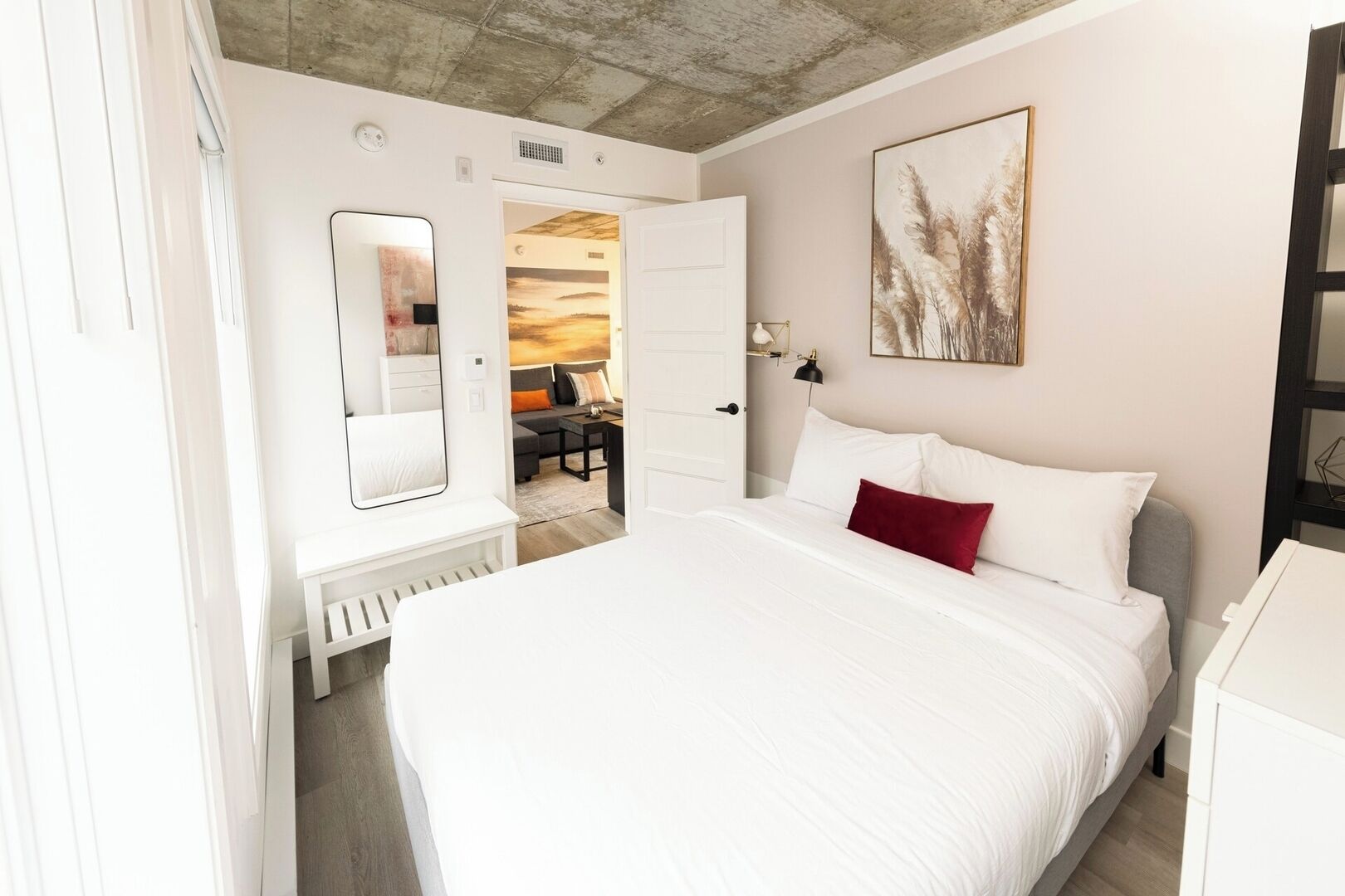 Un dormitorio con una cama grande, una mesita de noche, un espejo y una puerta que da a otra habitación.