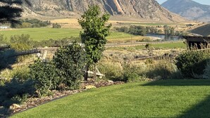Un paisaje montañoso con cielo despejado, un campo cubierto de hierba y un edificio pequeño en primer plano.