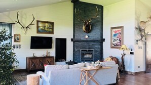 Un salón espacioso con chimenea, ciervos colgados en la pared y un ventilador de techo.