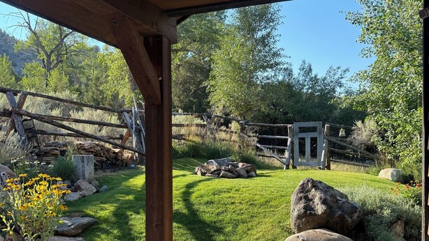 Una terraza de madera con vistas a un jardín ajardinado, que incluye un césped, rocas y una cerca de madera.