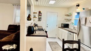 Une cuisine compacte équipée d’une cuisinière à gaz, d’un four à micro-ondes et d’un réfrigérateur. Une table à manger avec des chaises est placée au premier plan.