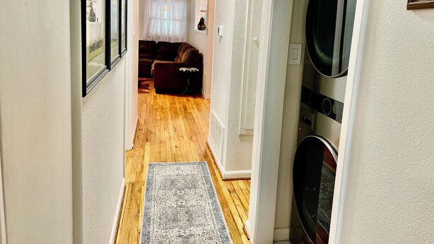 Un couloir avec un plancher en bois, un tapis, un canapé et un lave-linge.