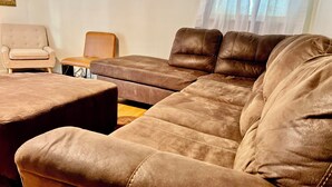 Un salon avec un canapé en cuir marron, un pouf assorti et une petite table.