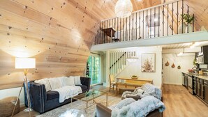 A spacious loft with a high ceiling, a dining area, a kitchen, and a staircase leading to an upper level. - Cozy A-Frame Retreat (Gatlinburg)