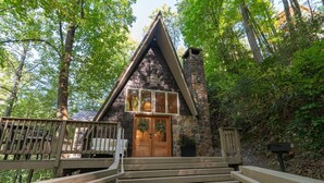 A wooden cabin with a stone chimney, a wooden deck, and a wooden door. - Cozy A-Frame Retreat (Gatlinburg)