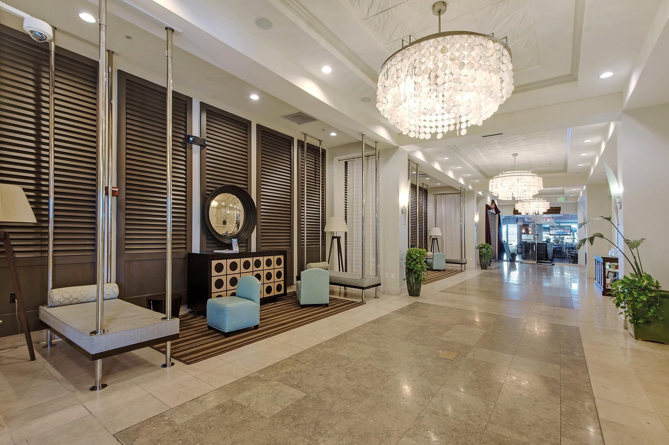 En moderne hotellobby med reception, siddeområde og en lysekrone.