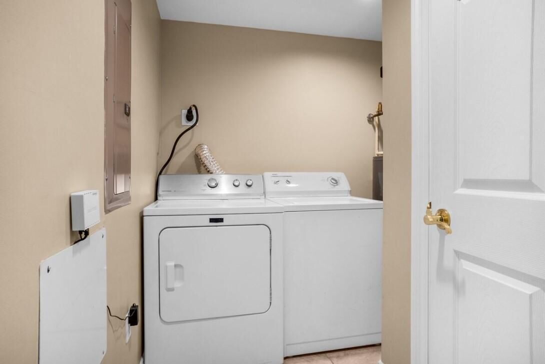 A laundry room with a washer and dryer, a wall-mounted heater, and a door with a brass handle.