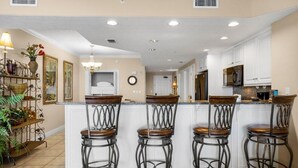 A kitchen with a central island, four bar stools, white cabinets, and a hanging light fixture.