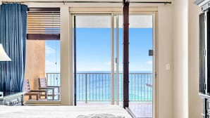 A hotel room with a large bed, a view of the ocean through a sliding glass door, and a balcony with chairs.