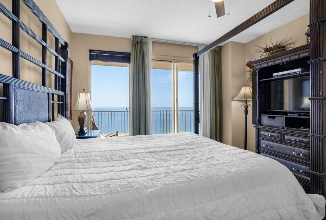 Habitación de hotel con una cama grande, televisión, cómoda y vista al mar desde un balcón.