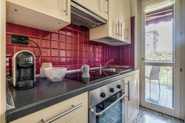 A kitchen with a red tiled backsplash, a coffee machine, a kettle, and a stove.