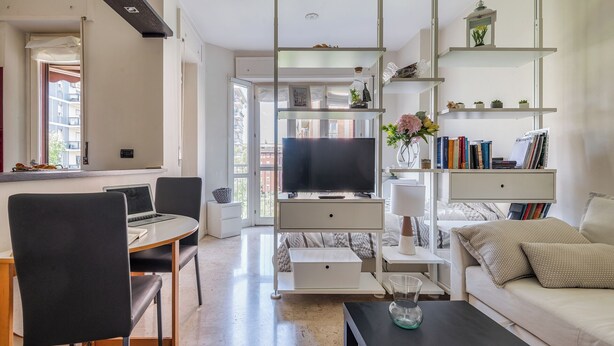 Un salon moderne doté d’un téléviseur à écran plat, d’un coin repas avec un ordinateur portable et d’un canapé agrémenté de coussins décoratifs.