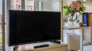 Un salon moderne avec un téléviseur à écran plat, une télécommande, une lampe, un vase de fleurs et des livres sur une étagère.