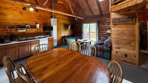 L’intérieur d’un chalet en bois comprend une table à manger, des chaises, un coin cuisine et un espace salon confortable avec un canapé et des fauteuils.