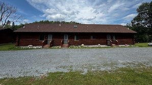 Une cabane en rondins avec une allée en gravier et une pelouse verdoyante.