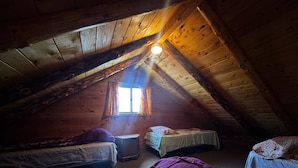 Une pièce mansardée chaleureuse, avec trois lits, un petit radiateur et une fenêtre avec des rideaux.