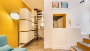 A modern interior with a staircase, a blue chair, and a white wall with framed artwork. - Garibaldi's Gem - La Vista Apartments (Milano)