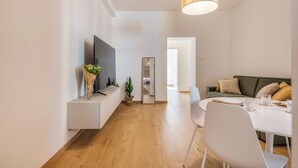 A modern living room with a flat-screen TV, a dining table with chairs, a sofa with cushions, and a large mirror. - New NoLo - La Vista Apartments (Milan)