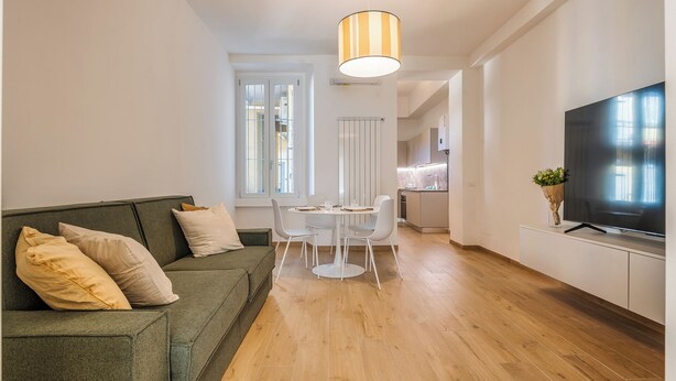 A modern living room with a green sofa, a dining table, and a TV on a white cabinet. - New NoLo - La Vista Apartments (Milan)