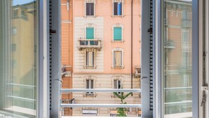 A view through a window of a building with multiple windows, some with shutters, and a balcony with a railing. - New NoLo - La Vista Apartments (Milan)