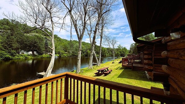 A wooden deck overlooking a lake with picnic tables and a covered area.