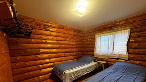 A log cabin room with two beds, a small table, and a window with curtains.