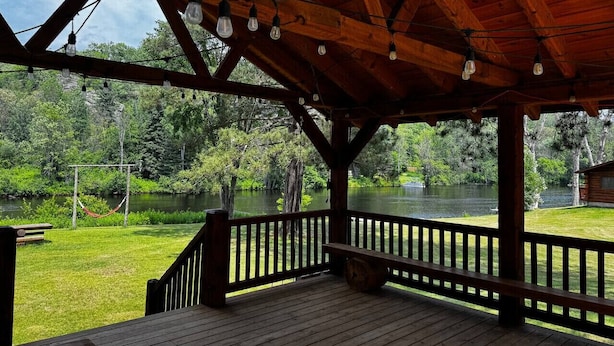 A wooden deck with a railing overlooking a lake, surrounded by greenery.