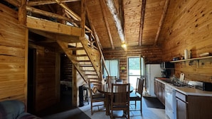 A rustic cabin interior with a wooden staircase, a dining area, and a kitchen.