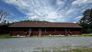 A log cabin with a gravel driveway and a grassy lawn.