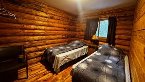 Una cabana amb dos llits, una panxa de darrera i una finestra amb cortines.