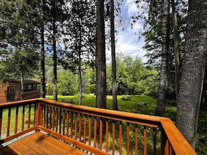 A wooden deck with a view of a lake and picnic tables in a forested area.