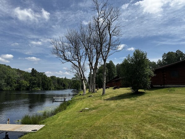 A lakeside cabin with a dock, surrounded by trees and a grassy area.