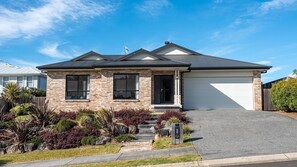 A two-story house with a garage, brick facade, and a well-maintained front yard with various plants and a driveway. - Holiday Crescent – Spacious, stylish retreat with pool, perfect (Berry)