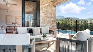 A modern living room with a sofa, chairs, and a coffee table. There is a large window with a view of a pool and mountains. - Holiday Crescent – Spacious, stylish retreat with pool, perfect (Berry)