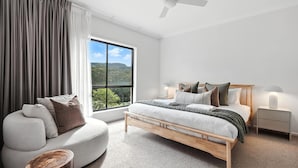 A modern bedroom with a large window, a bed with multiple pillows, a bedside table with a lamp, and a sofa with cushions. - Holiday Crescent – Spacious, stylish retreat with pool, perfect (Berry)