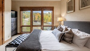 Una camera da letto con un letto, una panca, un comò e ampie finestre vista alberi.