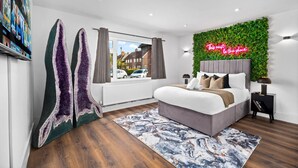 Een moderne slaapkamer met een bed, een groene wand, een neonbord en een raam met uitzicht op de straat.