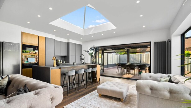Een moderne keuken met dakraam, een eethoek met tafel en stoelen, en een zithoek met bank en voetenbank.