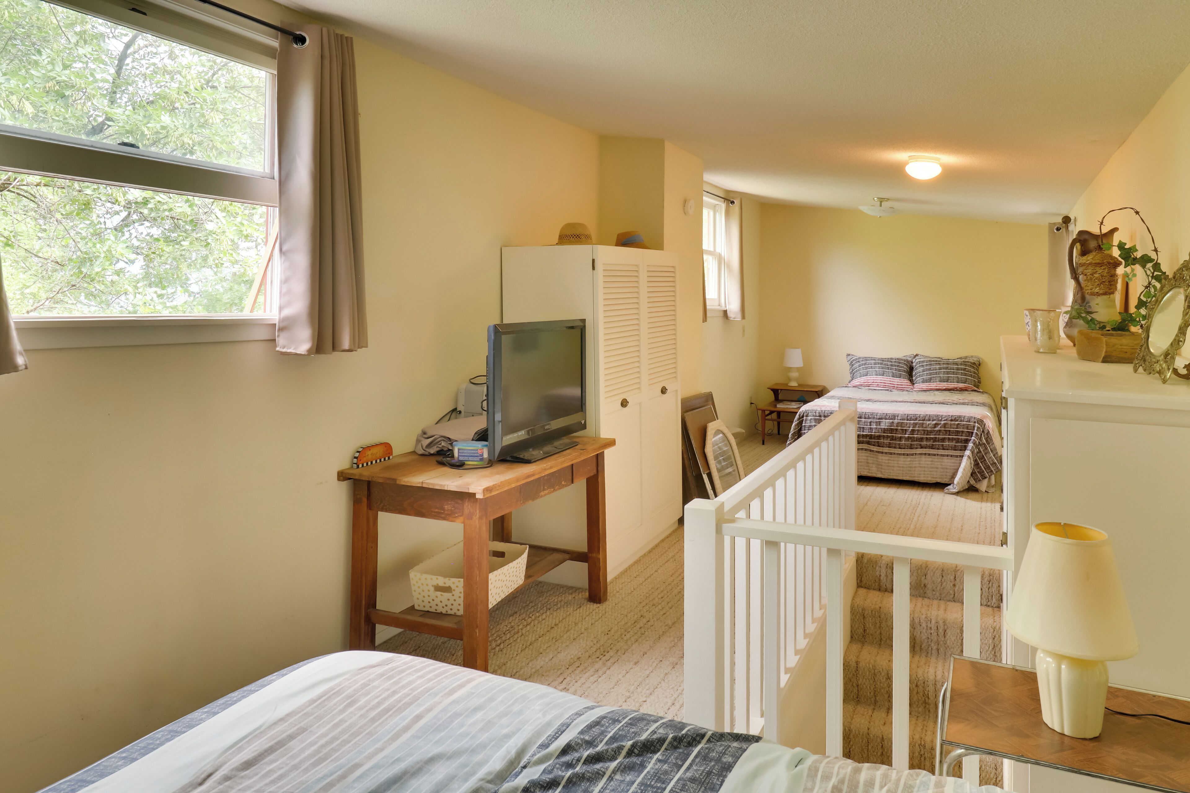 Ein Schlafzimmer mit einem Bett, einem Schreibtisch mit Fernseher, einem Kleiderschrank und einer Treppe, die in einen anderen Raum führt.