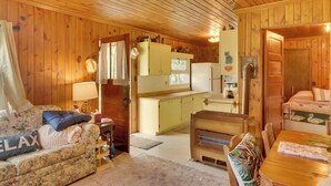 A cozy cabin interior with a wooden floor, a sofa with a 'RELAX' pillow, a dining table, a kitchenette, and a bed with a green and white pillow. - Pet-Friendly Vergas Cabin on Loon Lake w/ Dock! (Vergas)