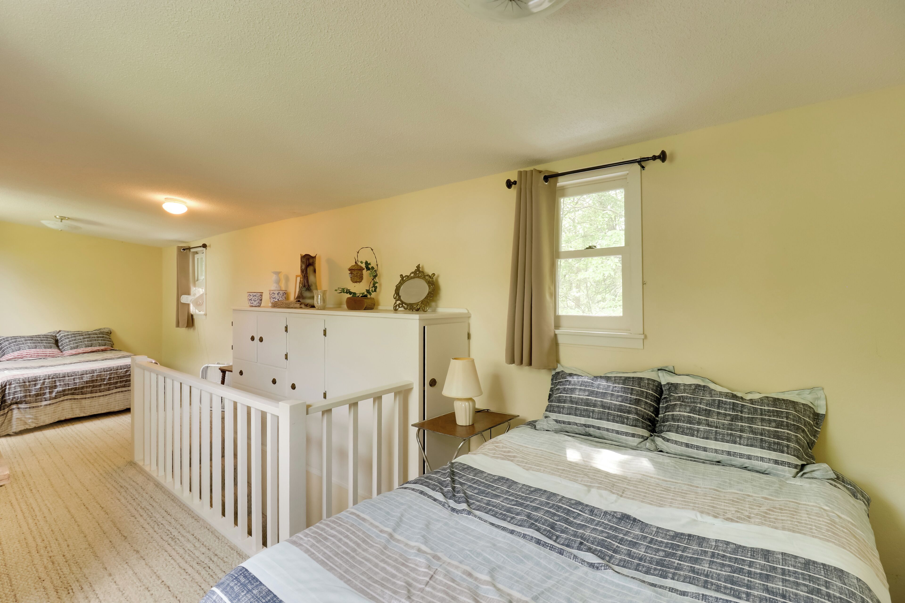 A bedroom with two beds, a dresser, a nightstand, a window with curtains, and a ceiling light.