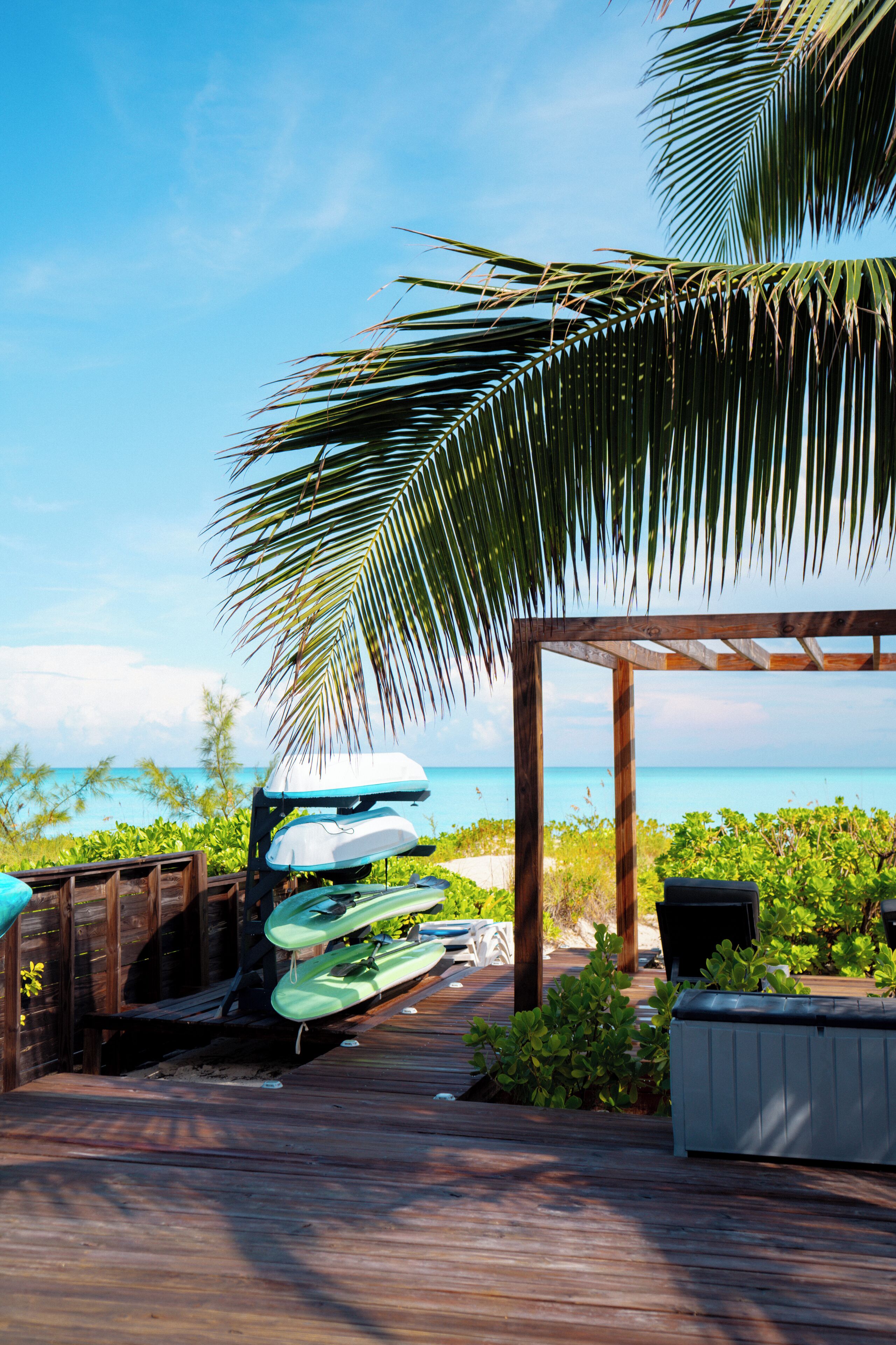 A wooden deck with kayaks and a covered seating area overlooking a beach.