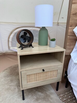 Una mesita de noche de madera con una lámpara, un ventilador y una pequeña planta.